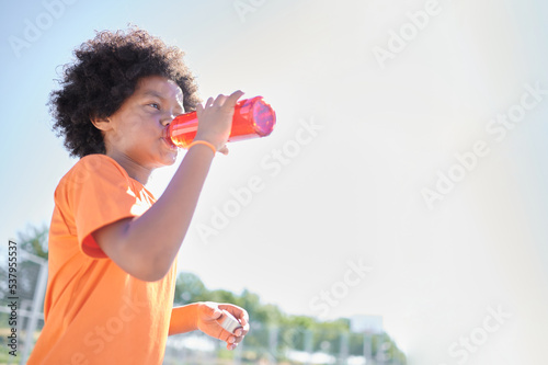 Young boy with afro hair wears the orange Netherlands national football team equipment while refreshes himself with water after playing football in a training field.