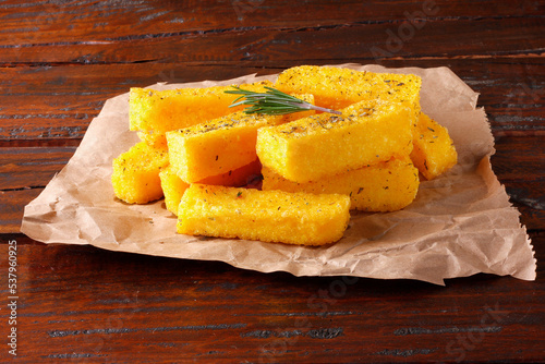 Fried polenta sticks in paper over rustic wooden table