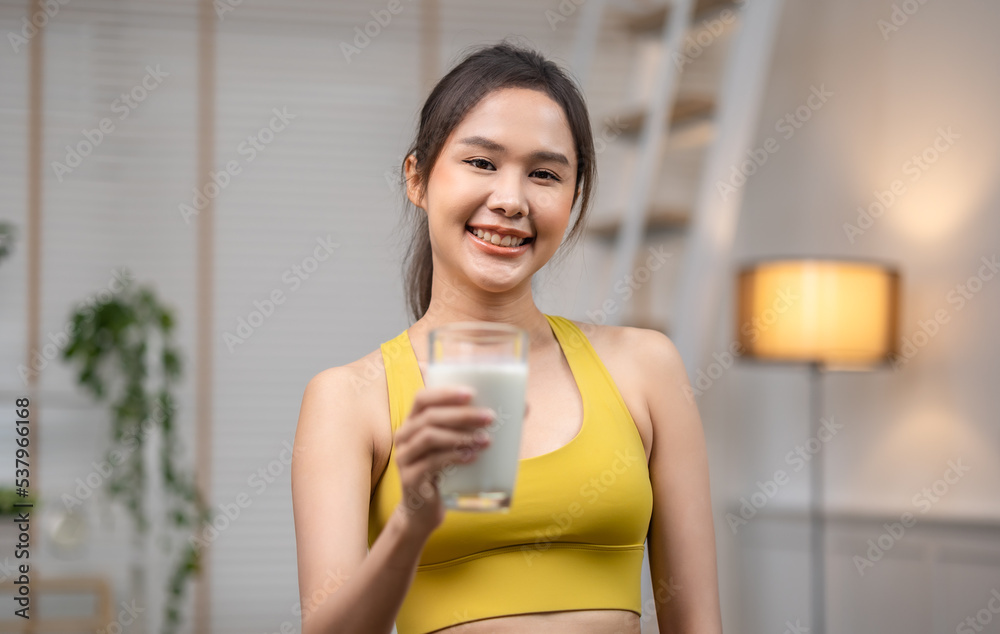 Attractive fitness asian woman finishing workout and drinking protein milk shake vitamins after training at home. Bodybuilding. Healthy lifestyle. Attractive fitness asian woman finishing workout and drinking protein milk shake vitamins after training at home. Bodybuilding. Healthy lifestyle.