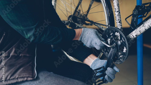 Close-up shot of strong male hands in protective gloves repairing broken bicycle treadle tightening loose joint with allen wrench in nice cozy workplace.