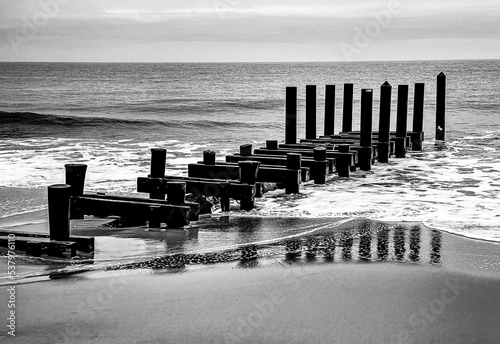 A Pier juts into the Atlantic Ocean off the coast of New Jersey, with the reflection visible as the waves recede