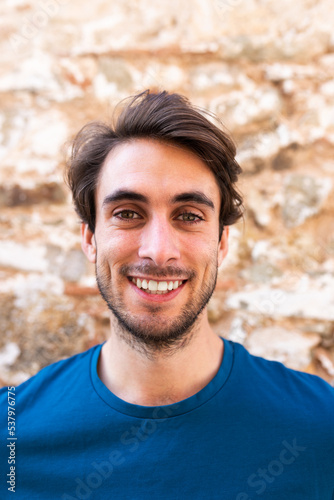 Portrait of happy young caucasian man looking at camera with brick stone background.