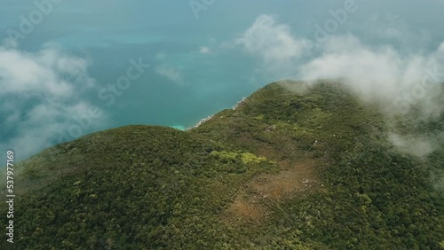 Drone aerial above clouds showing tropical forest on an island with blue water photo