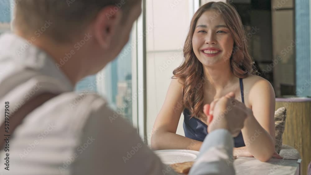 Young beautiful elegant asian female lady having a good time with her caucasian boyfriend eating lunch in a rooftop restaurant and lounge and her bf propose to her and put on engagement ring