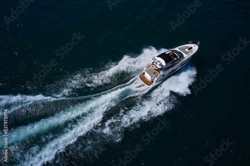 Aerial view of the sea and the boat. Luxurious large yacht with people moving quickly on dark blue water making a white trail behind the boat. Beautiful natural seascape in summer. © Berg