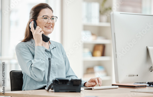 Telephone, computer and business woman in office, talking or conversation. Landline, receptionist and happy female from Canada in phone call, discussion or work call on desk in company workplace. photo