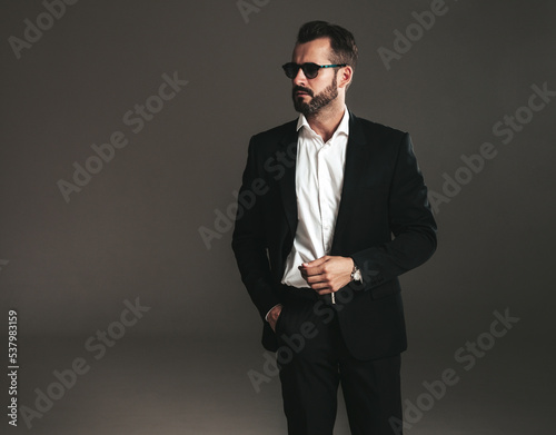 Closeup portrait of handsome confident stylish hipster lambersexual model. Sexy modern man dressed in elegant black suit. Fashion male posing in studio on dark background. In sunglasses