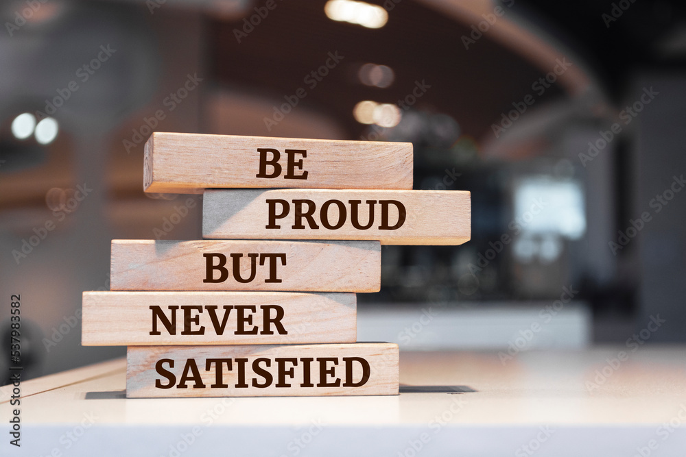 Wooden blocks with words 'Be proud but never satisfied'.