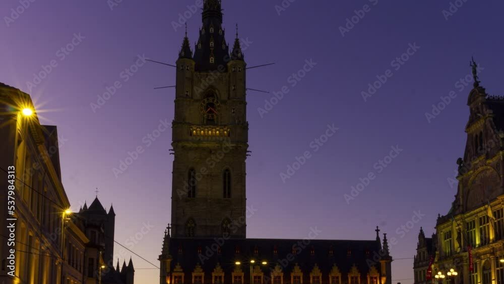 Time lapse of sun setting behind Belfort (Belfry) tower in Ghent, Belgium. day turns into night and lights of the buildings surrounding Sint-Baafsplein start burning. Tilt down to busy city square. Time lapse of sun setting behind Belfort (Belfry) tower in Ghent, Belgium. day turns into night and lights of the buildings surrounding Sint-Baafsplein start burning. Tilt down to busy city square.