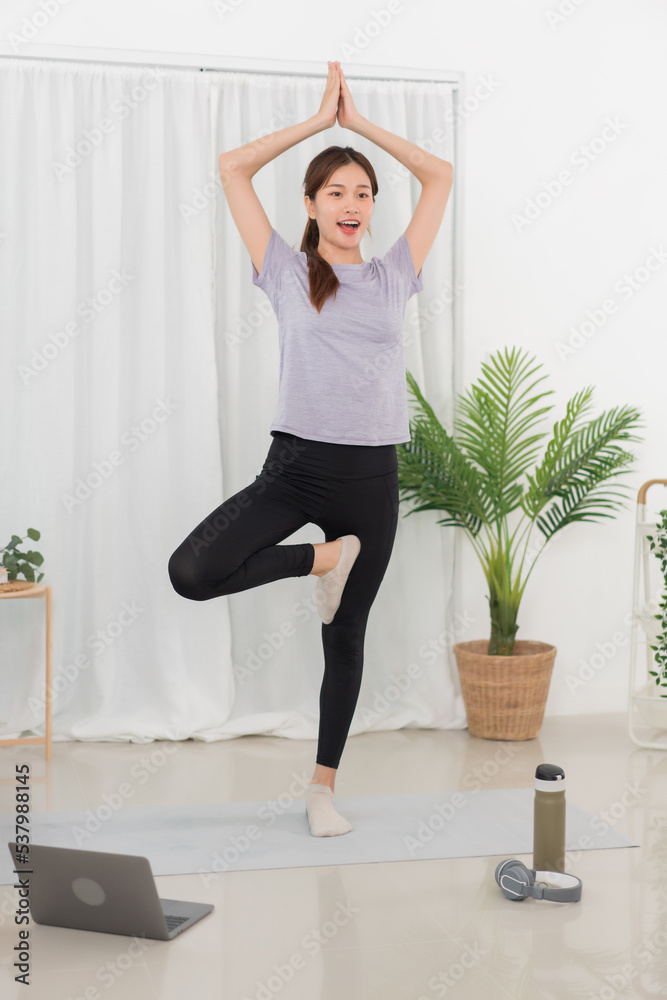 Yoga exercise concept, Asian woman standing to doing in tree pose and watching yoga tutorial online Yoga exercise concept, Asian woman standing to doing in tree pose and watching yoga tutorial online