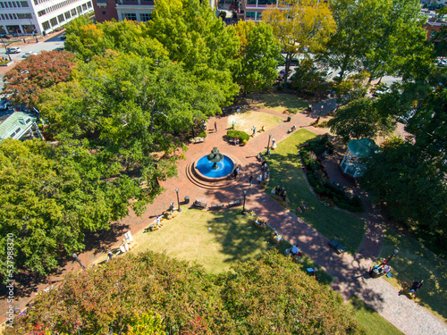 an aerial shot of a gorgeous autumn landscape at the Marietta Square with a water fountain surrounded by lush green trees and autumn colored trees with buildings and blue sky in Marietta Georgia USA photo