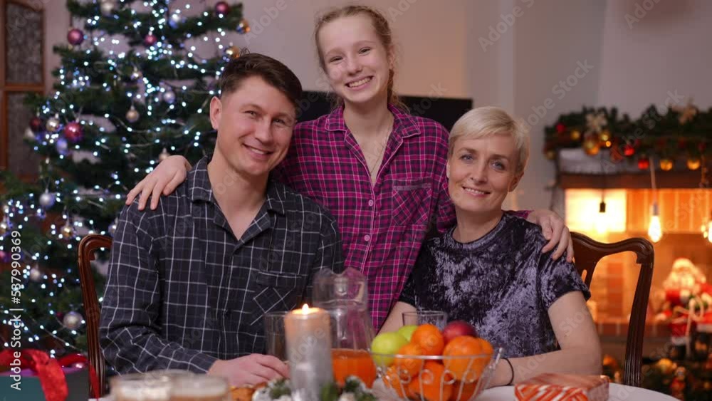 Charming teen daughter posing with father and mother sitting at dinner table at home on New Year's eve. Portrait of happy Caucasian confident girl man and woman looking at camera smiling Charming teen daughter posing with father and mother sitting at dinner table at home on New Year's eve. Portrait of happy Caucasian confident girl man and woman looking at camera smiling