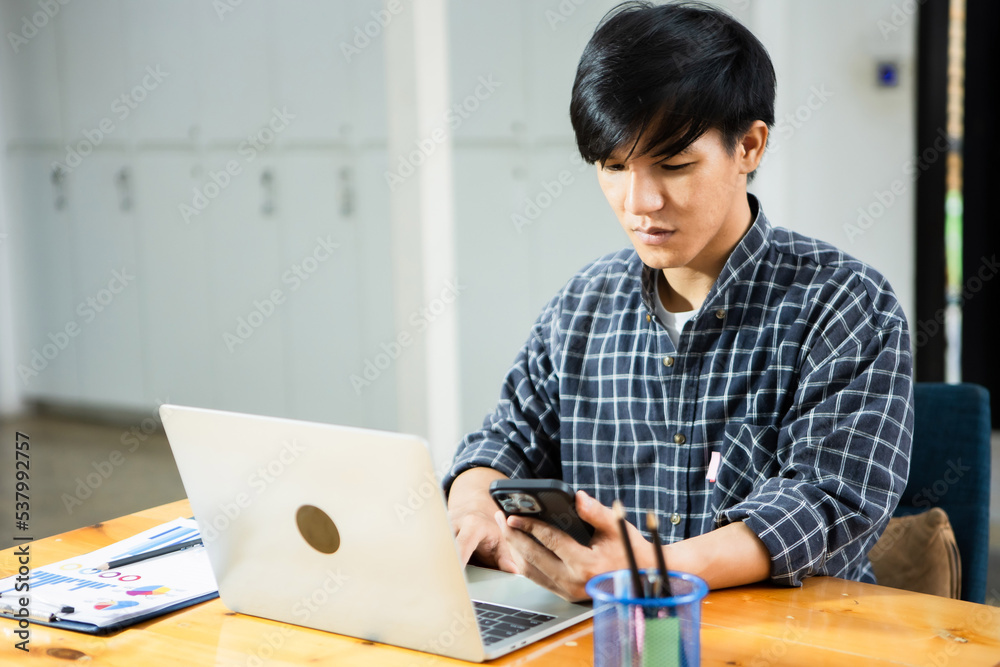 A young financial market analyst works in the office with his laptop while sitting at a wooden table. businessman analyzing graph document in hand. A young financial market analyst works in the office with his laptop while sitting at a wooden table. businessman analyzing graph document in hand.