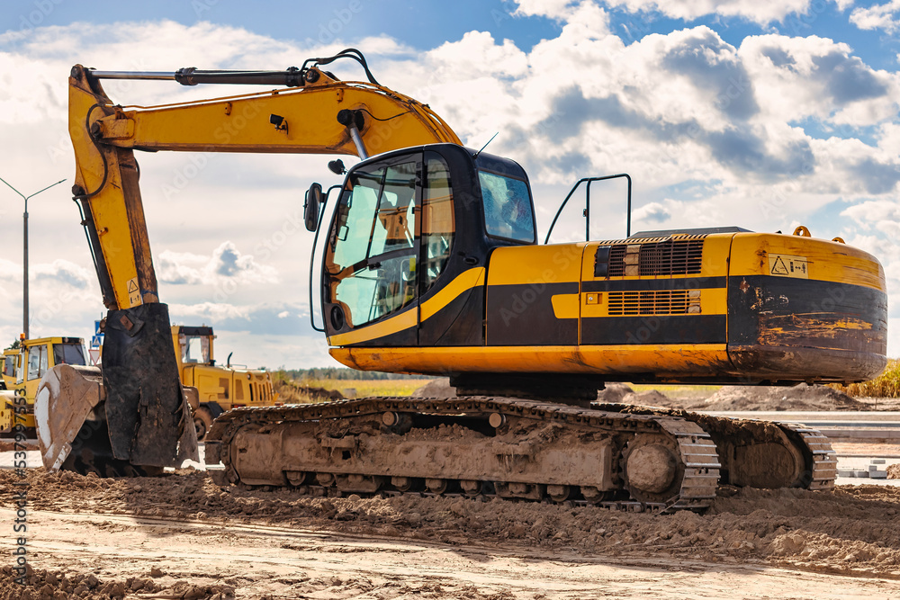 Powerful excavator at a construction site against a blue cloudy sky. Earthmoving equipment for construction. Development and movement of soil. Powerful excavator at a construction site against a blue cloudy sky. Earthmoving equipment for construction. Development and movement of soil.