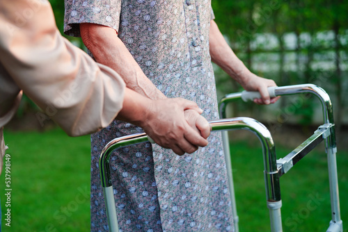 Caregiver help Asian elderly woman disability patient walk with walker in nursing hospital, medical concept. © manassanant