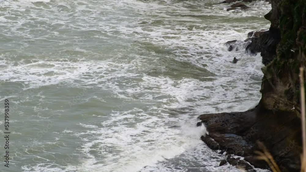 Waves crashing onto high dark cliffs during seabird's mating season in Muriwai, New Zealand Waves crashing onto high dark cliffs during seabird's mating season in Muriwai, New Zealand