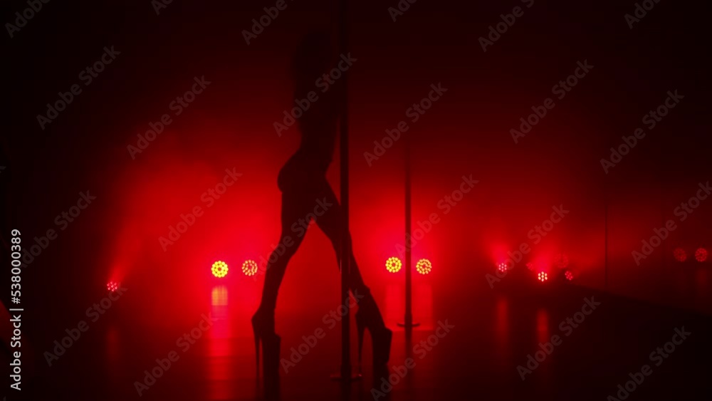 Slim woman performing poledance tricks sensually in spotlights. Sexy lady making moves upside down in night club. Young blonde dancer doing twine on pylon illuminated soft nightclub backlight.
