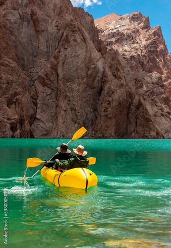Kayaking on a mountain lake. Two men are sailing on a red canoe along the lake along the rocks. The theme of water sports and summer holidays.