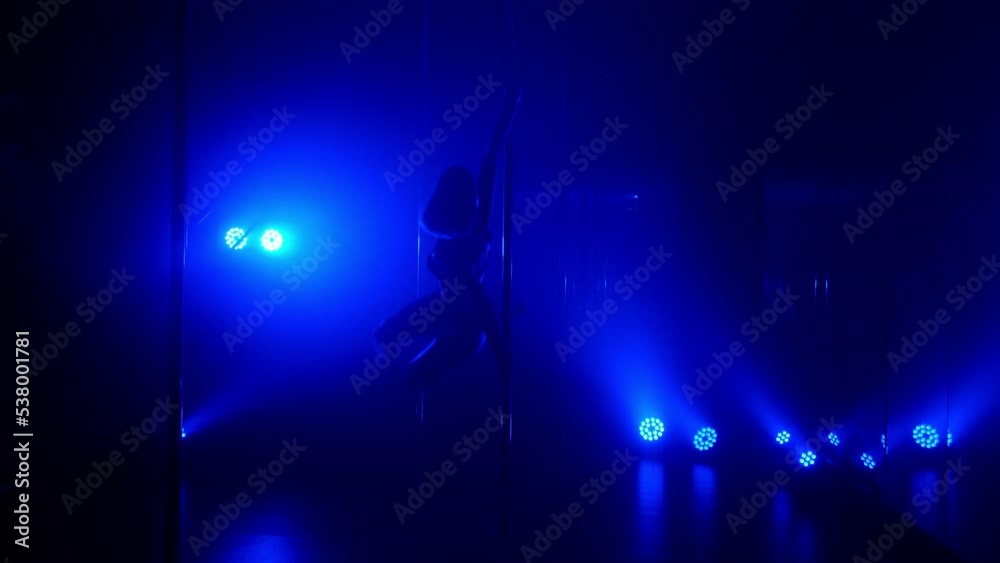 Slim woman performing poledance tricks sensually in spotlights. Sexy lady making moves upside down in night club. Young blonde dancer doing twine on pylon illuminated soft nightclub backlight.