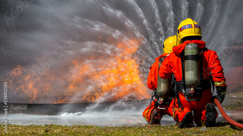 Asian firefighter on duty firefighting, Asian fireman spraying high pressure water, Fireman in fire fighting equipment uniform spray water from hose for fire fighting. © Kalyakan