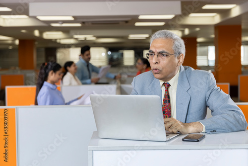 Displeased senior man using laptop at office.