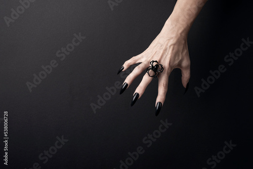 Reaching hand with long black nails and spider ring on a black background. Happy Halloween holiday concept