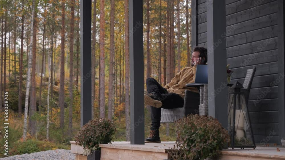 Man at home office, sitting outdoors talking on phone. Northern fall scene. Zoom in