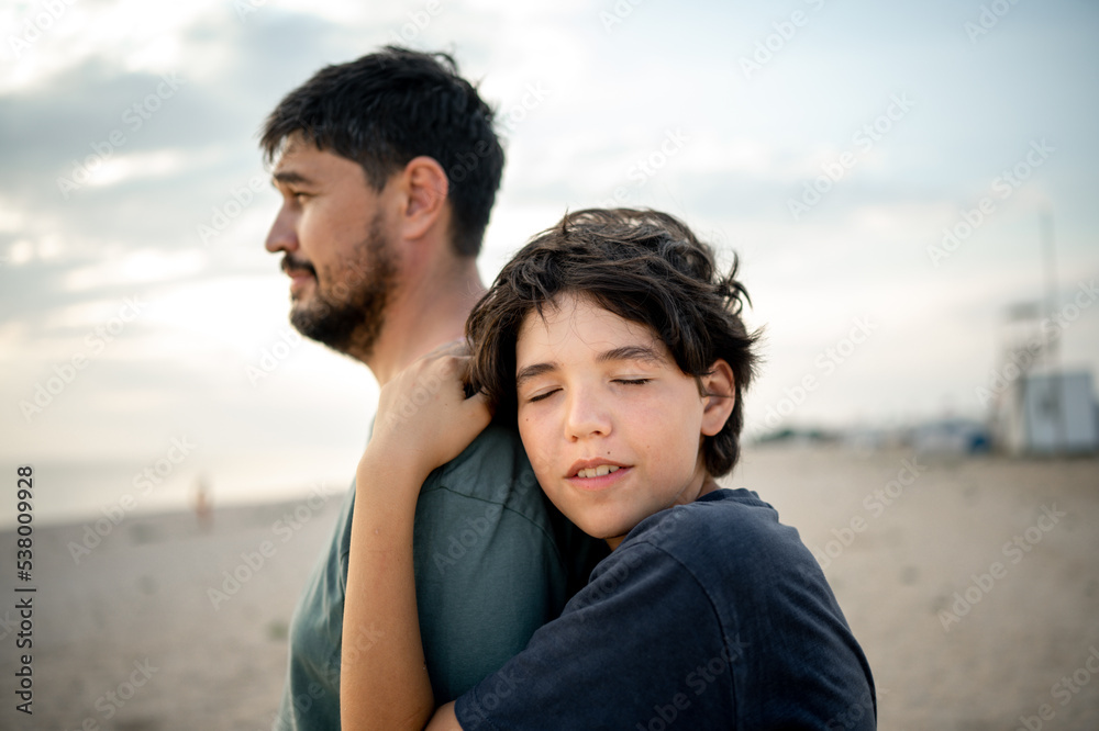 The teenage boy snuggles with tenderness to the strong shoulder of the father, the child seeks protection and support from the parents The teenage boy snuggles with tenderness to the strong shoulder of the father, the child seeks protection and support from the parents