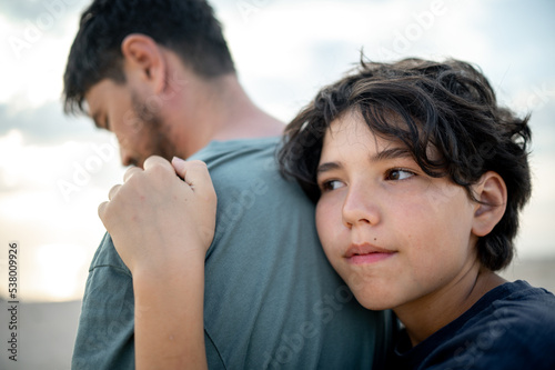 The teenage boy snuggles with tenderness to the strong shoulder of the father, the child seeks protection and support from the parents