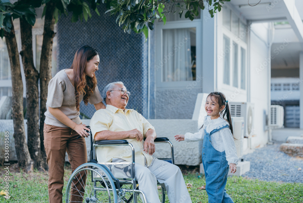 Fototapeta premium Disabled senior grandpa on wheelchair with grandchild and mother in park, Happy Asian multi generation family having fun together outdoors backyard, Grandpa elderly and little child smiling and laugh.