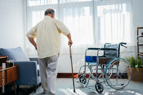 Asian senior old man with wheelchair walking with walker cane stick in nursing home, elderly mature disabled man patient, elderly health care concept. photo