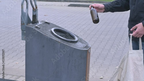 man throws a brown glass bottle into a glass container labeled 