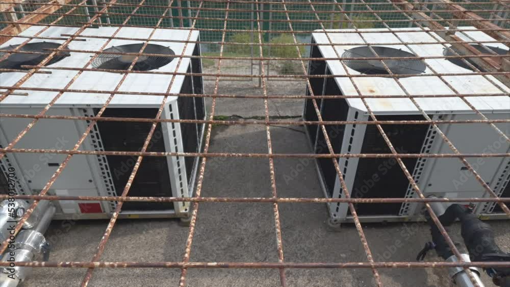 Air conditioning equipment - big outdoor heat exchange units containing pump (compressor) used for cooling and temperature control, in a wire mesh cage. 