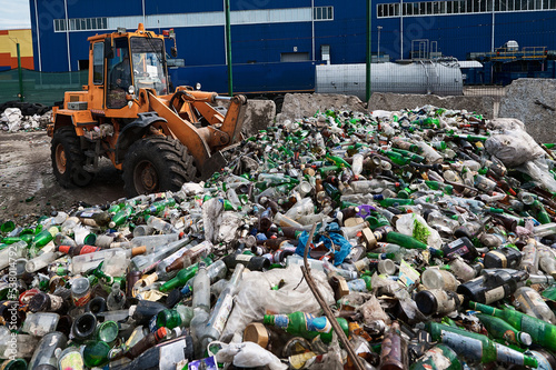 The bucket loader breaks glass bottles by dumping them out of the bucket. Preparing glass containers for recycling