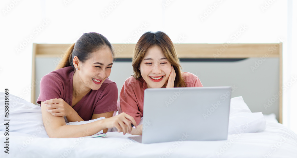 Millennial Asian young happy cheerful female teenager LGBTQ lesbian lover couple laying down together on bed and pillow learning studying online via laptop computer and writing short note on notebook Millennial Asian young happy cheerful female teenager LGBTQ lesbian lover couple laying down together on bed and pillow learning studying online via laptop computer and writing short note on notebook