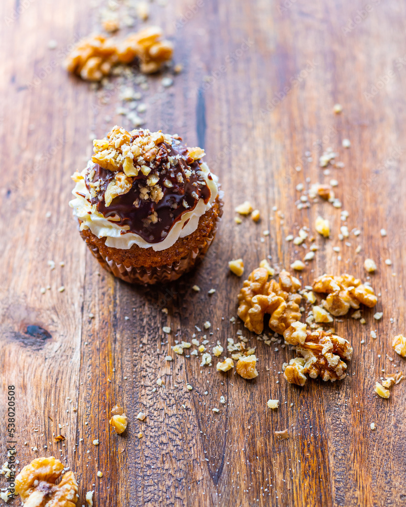 Tasty chocolate muffin with creme mascarpone and chocolate on top, covered with nuts. Placed on wooden desk. Sweet fresh and homemade cupcake. Tasty chocolate muffin with creme mascarpone and chocolate on top, covered with nuts. Placed on wooden desk. Sweet fresh and homemade cupcake.
