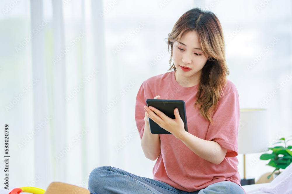 Millennial Asian young happy cheerful thoughtful female teenager sitting smiling on cozy bed in bedroom at home thinking holding notebook writing note checking clothes preparing for weekend vacation Millennial Asian young happy cheerful thoughtful female teenager sitting smiling on cozy bed in bedroom at home thinking holding notebook writing note checking clothes preparing for weekend vacation