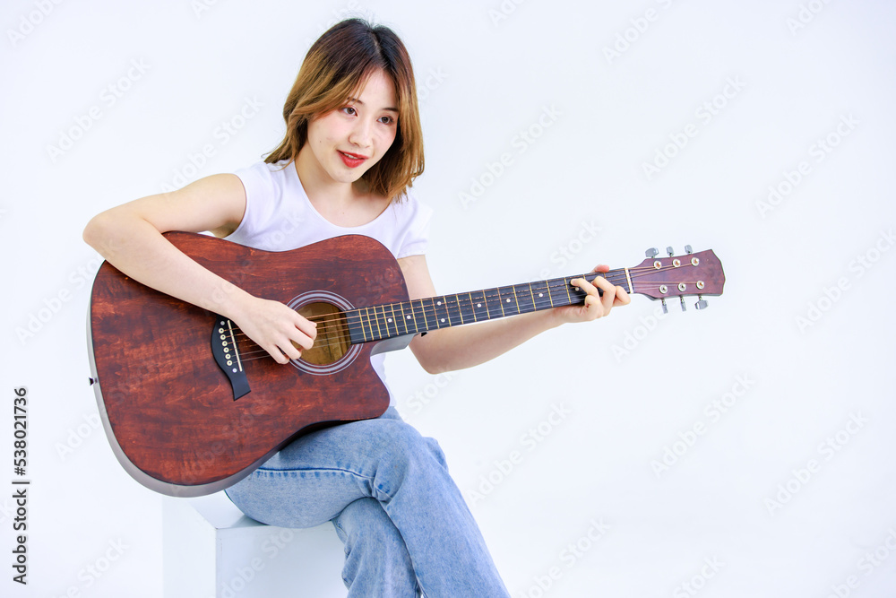Isolated cutout studio full body shot of Millennial Asian young happy cheerful female teenager teen model in casual outfit sitting on square box smiling singing playing guitar on white background Isolated cutout studio full body shot of Millennial Asian young happy cheerful female teenager teen model in casual outfit sitting on square box smiling singing playing guitar on white background