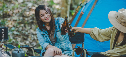 Young women sitting and drink beverage front of camping tent