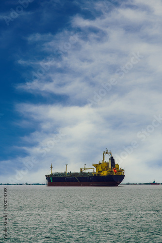 Day view of moored cargo ship at a calm sea against blue sky with dense white clouds.