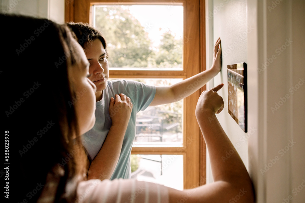 Mother and daughter using home automation through digital tablet mounted on wall at home Mother and daughter using home automation through digital tablet mounted on wall at home