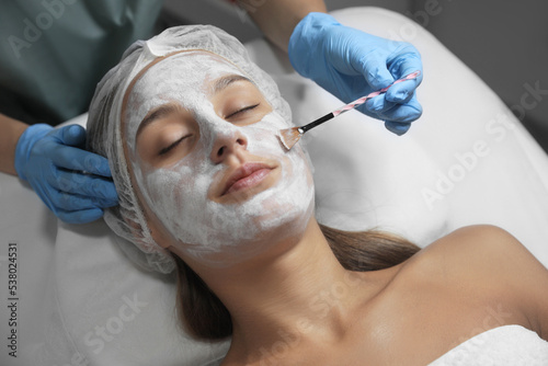 Cosmetologist applying mask on client s face in spa salon