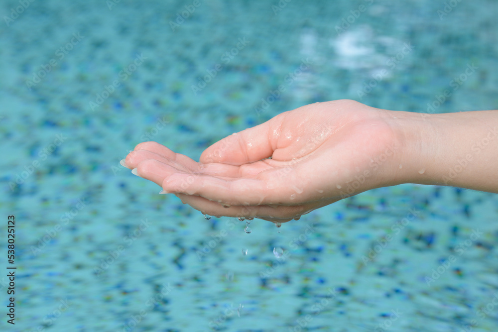 Girl holding water in hand above pool, closeup