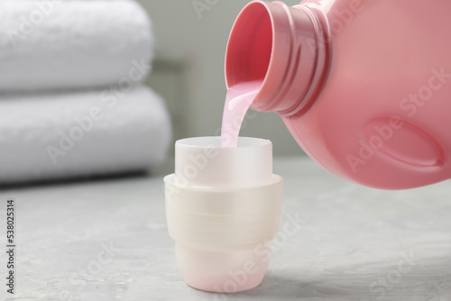 Pouring laundry detergent from bottle into cap on light grey marble table, closeup photo