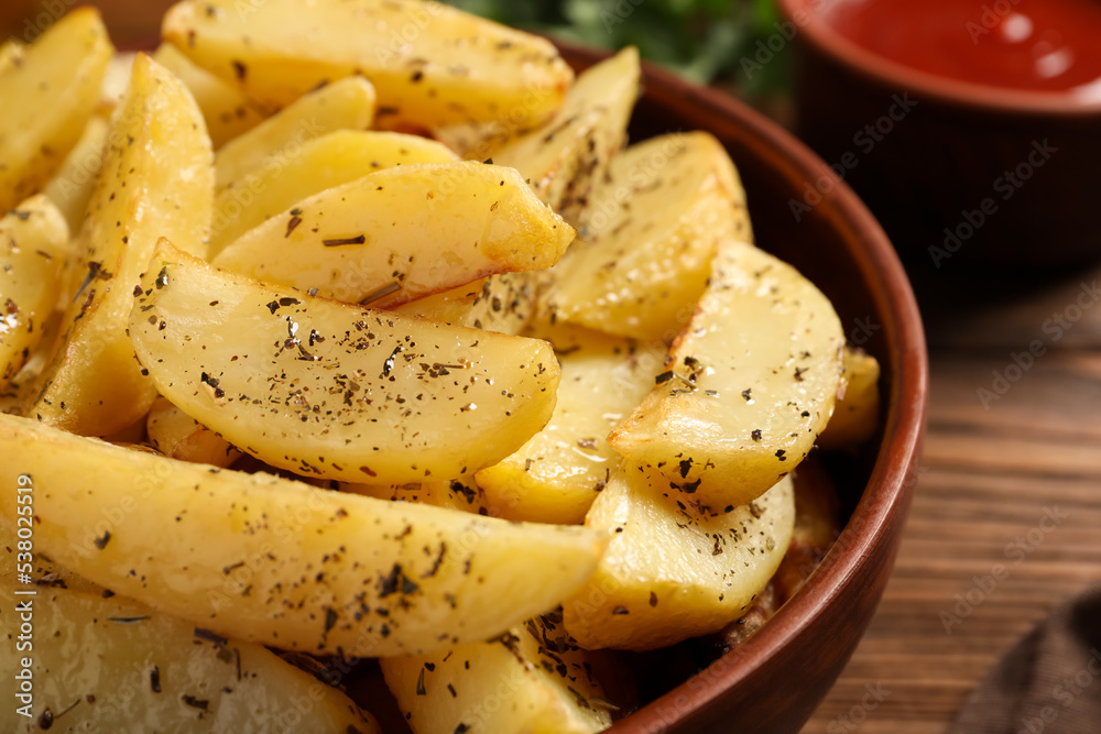 Bowl with tasty baked potato wedges and spices on wooden table, closeup Bowl with tasty baked potato wedges and spices on wooden table, closeup