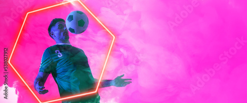 Caucasian male player balancing ball on chest over illuminated hexagon shape against pink background