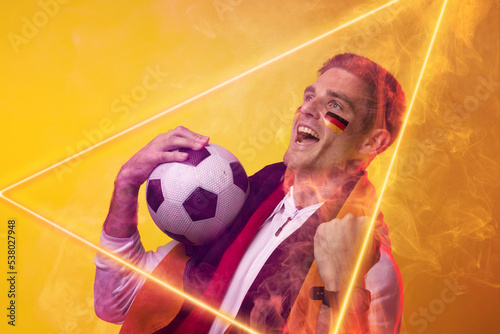 Male caucasian player holding german flag and ball screaming over illuminated triangle, copy space
