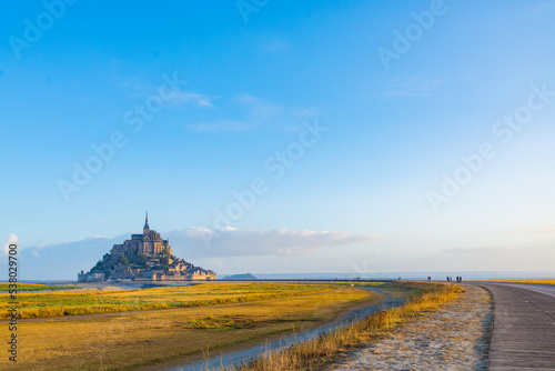 The famous "Mont Saint Michel", Normandy, France, with tourists walking on the pedestrian road. Blue sky on the background. With copy-space.