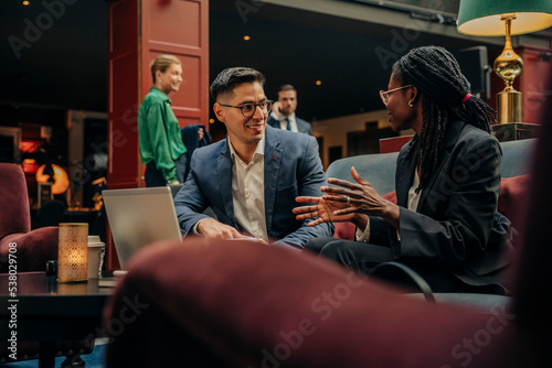 Smiling businessman looking at female colleague discussing while sitting in hotel lounge