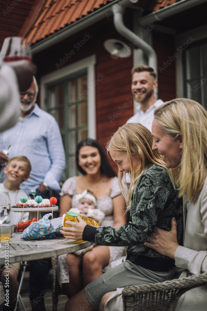 Side view of daughter looking at gift while sitting on mother's lap during birthday Side view of daughter looking at gift while sitting on mother's lap during birthday